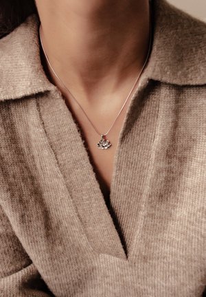 Silver necklace with a lotus flower pendant, worn against a textured, beige knitted sweater with a V-neck design.