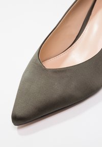 Chaussure plate pour femme à bout pointu en tissu vert olive mat avec doublure intérieure beige et détail de couture autour de l'ouverture.