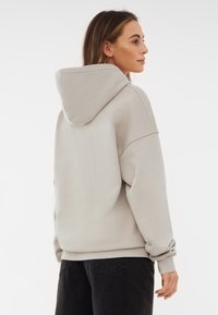 Jasnoszara, oversize'owa bluza z dużym kapturem, ściągaczami na rękawach i luźnym krojem. Gładka faktura, minimalistyczne detale szwów, noszona z ciemnymi spodniami.
