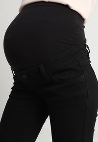 Jeans da maternità neri con cintura elastica, caratterizzati da una texture liscia e una vestibilità aderente. Il design consente comfort e adattabilità durante la gravidanza.