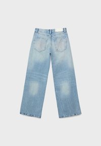 Jeans larges bleu clair posés à plat, montrant les poches arrière avec une légère usure et une étiquette blanche sur la ceinture.