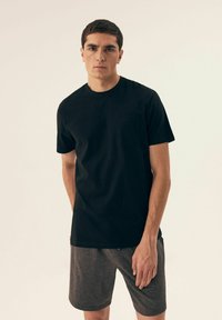 Czarny t-shirt z krótkim rękawem, okrągłym dekoltem i kieszonką na piersi, wykonany z teksturowanej tkaniny, zestawiony z ciemnoszarymi szortami.