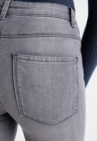 Sivi denim hlače z rahlo teksturirano površino, ki imajo zadnji žep s prepognjenim robom in minimalnimi šivi.