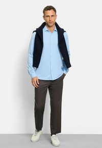 Helles blaues Hemd mit Knopfleiste, dunkler marineblauer Strickpullover, über die Schultern gelegt, graue Hose und weiße Sneaker. Strukturiertes Gewebe und taillierte Passform.