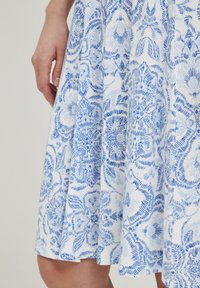 Vestido acampanado de algodón blanco con estampados florales azules, que presenta un diseño texturizado y un dobladillo que termina justo por encima de la rodilla.