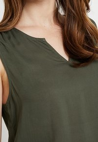 Olive green sleeveless top with a V-neckline. Made from a lightweight fabric with a smooth texture, featuring soft draping along the shoulders.