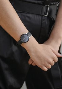 Fekete óra kerek számlappal és minimalista dizájnnal. Fekete szilikon szíjjal rendelkezik és egyszerű ezüst órajelzőkkel van ellátva.