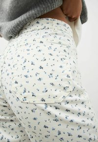 Witte broek met bloemenpatroon in blauw en zwarte accenten, voorzien van een hoge taille, achterzakken en een zachte stof. 