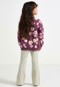 Lilla sweater med pink og beige blomster mønstre, parret med lysegrønne fløjlslækkede bukser. Blødt stof, afslappet design.