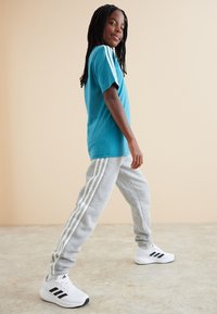 Teal t-shirt with white stripes on shoulders, paired with gray sweatpants featuring three white stripes. White sneakers with black accents.