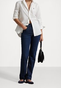 Bílá košile s dlouhým rukávem, tmavě modré džíny a námořnické baleríny. Černá kabelka s uzávěrem. Kalhoty mají rovný střih s decentními švy.