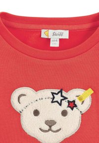 Rode t-shirt met een ontwerp van een witte teddybeer gezicht. Geborduurde sterren en een gele accenten op het hoofd van de beer voegen detail toe. Gemaakt van zacht katoen.