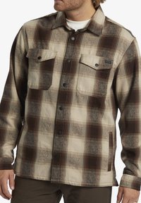 Bruine en beige geruite button-up jas gemaakt van textiel met een gestructureerde stof, met twee borstzakken, zwarte drukknoopsluitingen en een zijzak.
