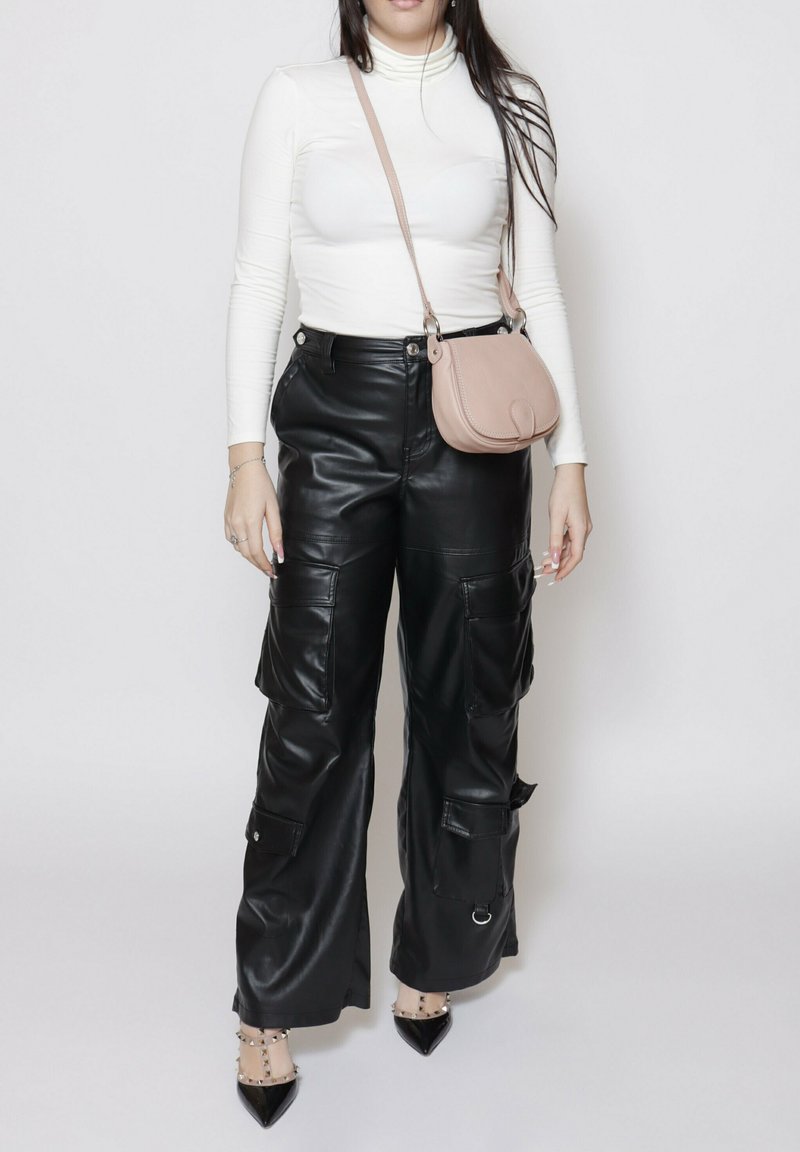 Pantaloni cargo in pelle nera con molte tasche, abbinati a un top fitted bianco a maniche lunghe e una piccola borsa a tracolla rosa. Tacchi neri.