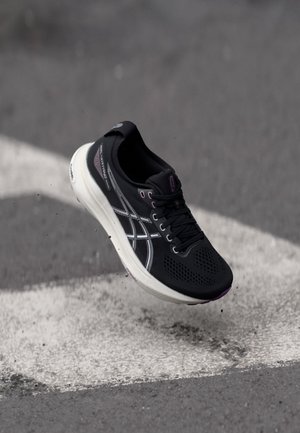 Pantofii sport negri au un superior din plasă respirabilă, accente reflectorizante argintii și o talpă albă cu detalii violet, concepuți pentru performanță.