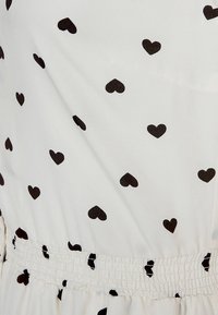 Tessuto bianco con motivo a cuori neri, caratterizzato da un dettaglio in vita arricciato. Texture morbida, design casual adatto a varie occasioni.