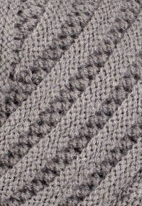 Tessuto in maglia grigio con motivo diagonale caratterizzato da texture in rilievo e piccoli spazi, che mette in evidenza una consistenza morbida e pelosa.