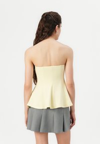 Strapless yellow peplum top with a fitted bodice and flared hem, paired with a gray pleated mini skirt. Smooth texture, simple design.