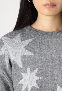 Pulover gri tricotat cu modele mari de stele albe, guler rotund și țesătură texturată. Design casual cu un aspect moale.