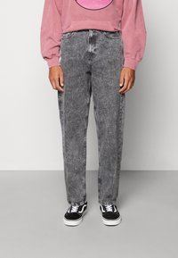 Pantalones de mezclilla gris con un corte recto, que presentan una textura desvaída y un diseño clásico de cinco bolsillos, combinados con zapatillas negras y blancas.