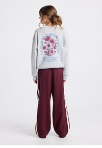 Sudadera gris con un gráfico floral en burdeos y texto azul en la parte trasera. Combina con pantalones holgados burdeos con rayas blancas en los laterales.