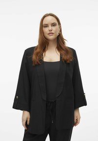 Černý blazer s šálovým límcem, dlouhými rukávy a akcenty ve zlaté barvě. Hladká látka a volný střih. Nesený přes černý top.