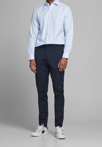 Jasnoniebieska koszula z długim rękawem, zestawiona z ciemnoniebieskimi spodniami i białymi sneakersami z czerwonymi oraz ciemnoniebieskimi akcentami.