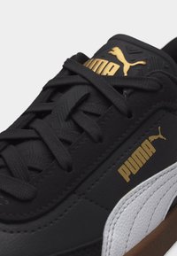 Ασπρόμαυρο παπούτσι Puma με μαύρα κορδόνια και χρυσό λογότυπο Puma στη γλώσσα και στην πλευρά, με εμφανές ανάγλυφο περίγραμμα στην σόλα.