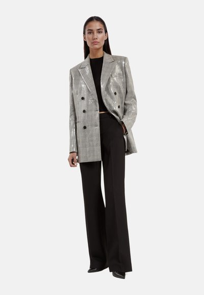 Zilveren pailletten dubbelknoop blazer met een gestructureerd ontwerp. Gecombineerd met zwarte wijde broek en een strakke zwarte top.