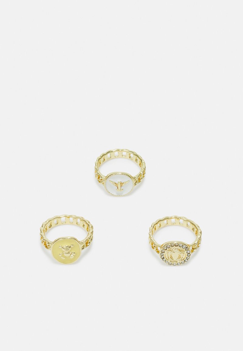 Conjunto de três anéis em tom dourado com configurações circulares. Um tem um logotipo, outro apresenta um design de urso e o último está adornado com strass.