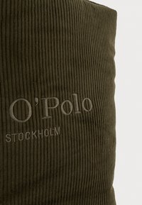 Coussin ribbé vert foncé avec un brodé "O'Polo" et le texte "STOCKHOLM" dans une teinte plus claire, mettant en avant un tissu texturé.