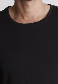 T-shirt nera a girocollo realizzata in tessuto misto cotone. Texture liscia con una forma aderente e dettagli di cucitura minimi.