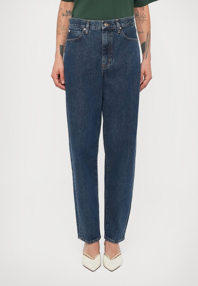 Τζιν παντελόνια με ψηλή μέση, ίσια γραμμή, σκούρο μπλε χρώμα και εμφανείς ραφές. Συνδυασμένα με κρεμ χρωματιστά μυτερά τακούνια.