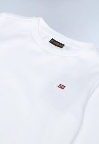 Sudadera de algodón blanco con cuello redondo y pequeño detalle bordado de la bandera noruega en el lado izquierdo del pecho. Textura suave, diseño sencillo.