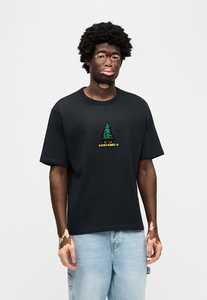 T-shirt nera in cotone con scollatura rotonda, con un disegno di un albero ricamato in verde e la scritta "Converse" in giallo sotto di esso.
