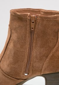 Bruine suède enkellaars met een zijrits, textuur op het oppervlak en een gestapelde hak. Beschikt over gestikte details en een ronde neus.