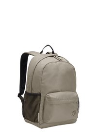 Sac à dos en tissu beige avec un compartiment principal, une poche avant et une poche latérale en mesh ; présente des accents noirs et une poignée supérieure.