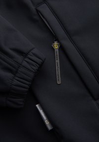 Manche de veste noire avec poignets élastiques et poche zippée avec une languette noire étiquetée "onblue performance" en texte jaune et noir.