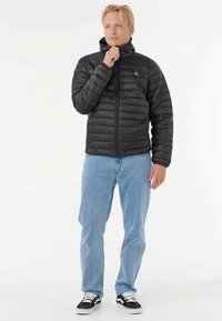 Black padded jacket with a stand-up collar, zippered front, and lightweight material, paired with light blue jeans and black sneakers.