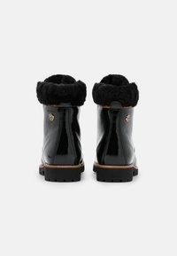 Stivaletti alla caviglia in pelle sintetica nera con risvolto in pelliccia finta, dettagli in oro e suola in gomma nera resistente. Finitura liscia e altezza media.