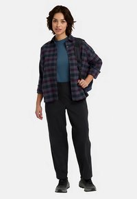 Kariertes Flanellhemd in Marineblau und Burgunderrot über einem türkisfarbenen Oberteil, kombiniert mit schwarzen Hosen und grauen Turnschuhen. Ausgestattet mit einem schwarzen Rucksack.