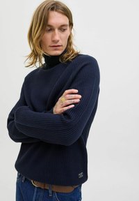 Navy ribbed turtleneck sweater featuring long sleeves, a relaxed fit, and a logo tag on the lower hem. Textured knit material.