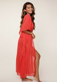 Kimono rojo, transparente, con un patrón geométrico, de frente abierto y mangas sueltas, que presenta una abertura lateral para facilitar el movimiento.