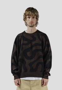 Pull à motifs marron et noir avec une coupe décontractée, un col côtelé et des manches raglan. Confectionné dans un tissu doux et texturé.