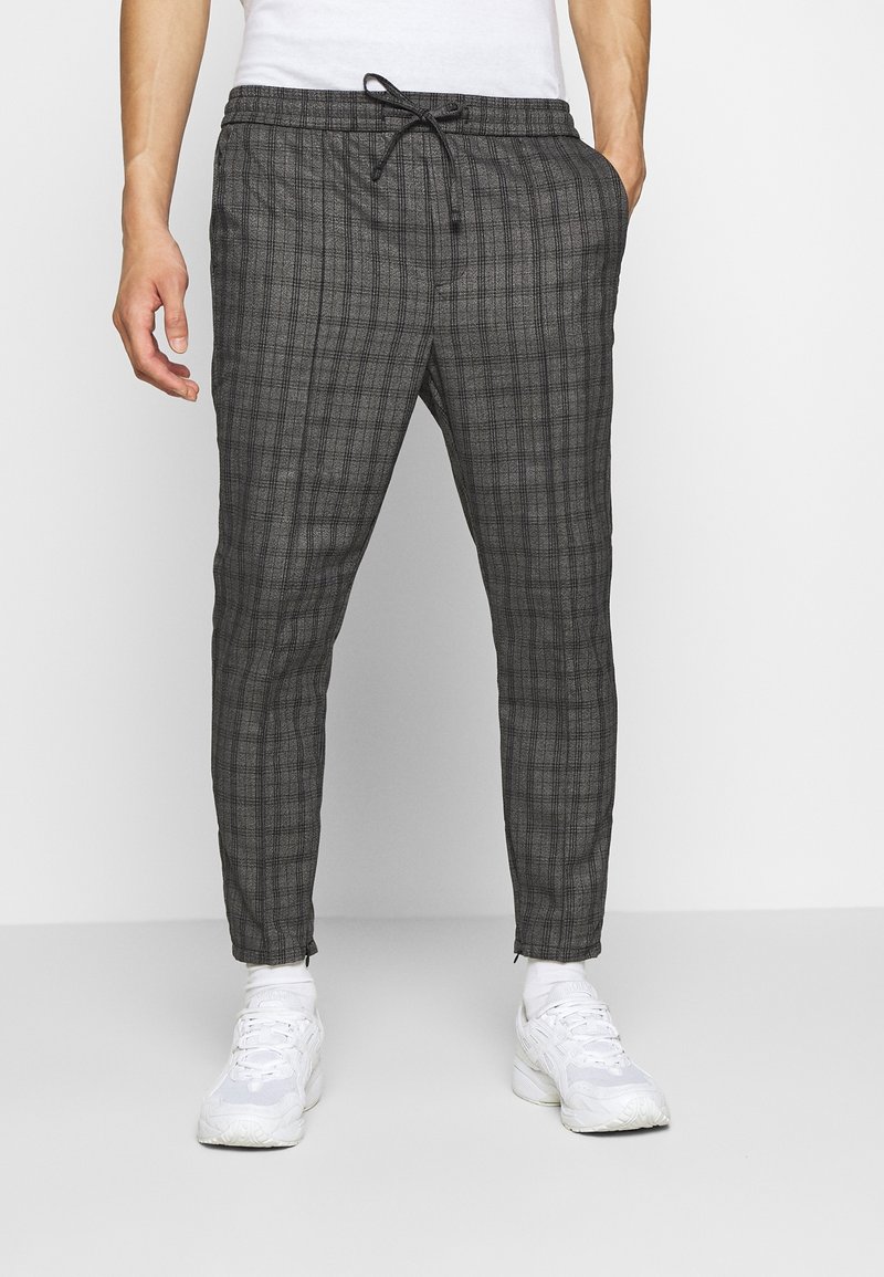 Grå rutiga jogger-byxor med elastisk midja och snörning, med sidofickor och avsmalnande anklar, i kombination med vita sneakers.