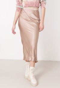 Gonna midi in satin beige con una texture liscia, caratterizzata da una vita alta e una fessura laterale, abbinata a stivali bianchi con lacci spessi.