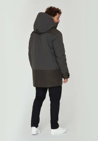 Puffjacka i mörkgrått och olivgrönt, med stor huva, dragkedja och texturerade material. Matchad med svarta byxor och vita skor.