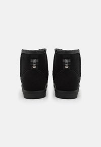 Botas de tobillo de ante negro con una textura suave, punta redonda y suela de goma plana. Incluyen tiradores de tejido en la parte trasera.