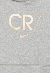 Szara bluza z miękką fakturą. Na przodzie duża, złota grafika "CR7" oraz małe logo Nike, oba wyraźnie widoczne.
