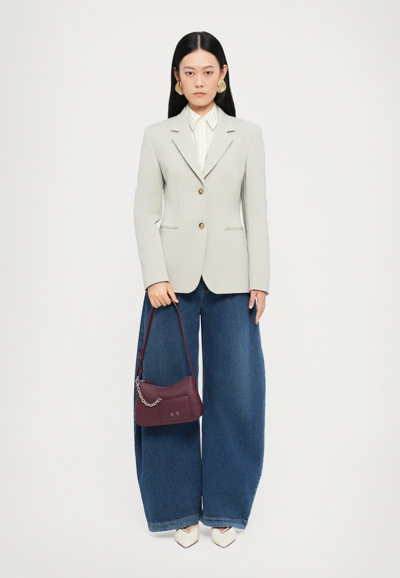 Blazer léger gris clair sur mesure avec des boutons dorés, associé à un pantalon en denim à jambes larges. Sac à main bordeaux avec détail en chaîne et chaussures à bouts pointus crème.